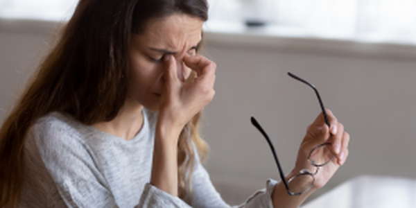 Tired woman holding glasses in left hand and pinching bridge of nose with her right hand